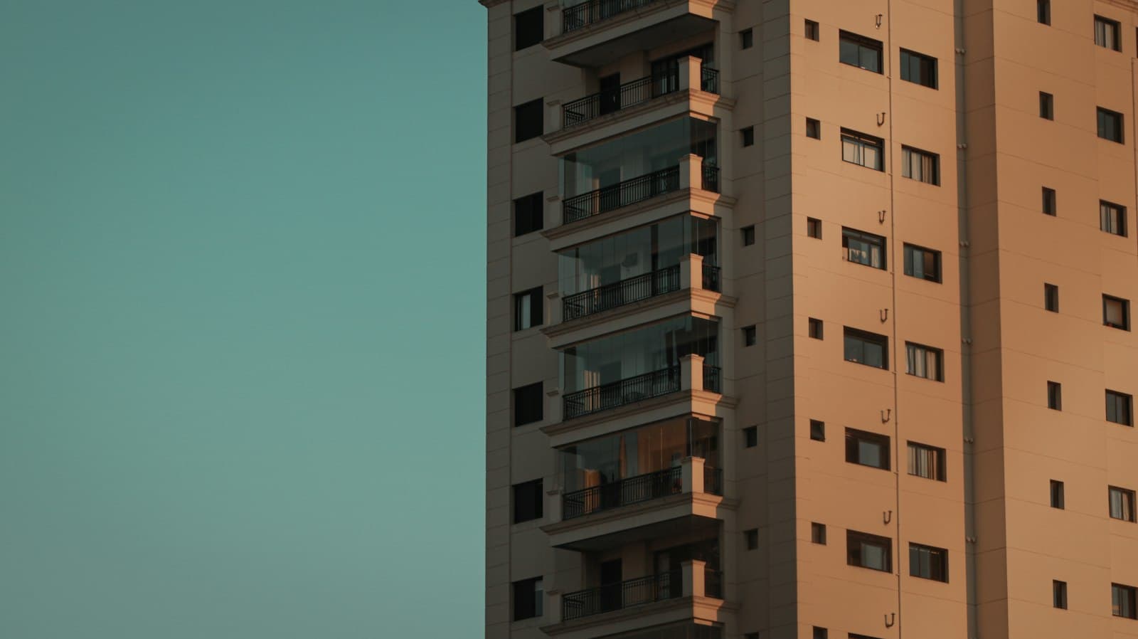 Prédio residencial de tom terroso contra um céu azul esverdeado